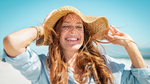 Woman smiling in summer sun on beach wearing straw hat - summer skin and collagen health
