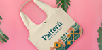A branded tote bag for "Pattern Wellness" featuring their logo and a nature-inspired design against a pink backdrop.