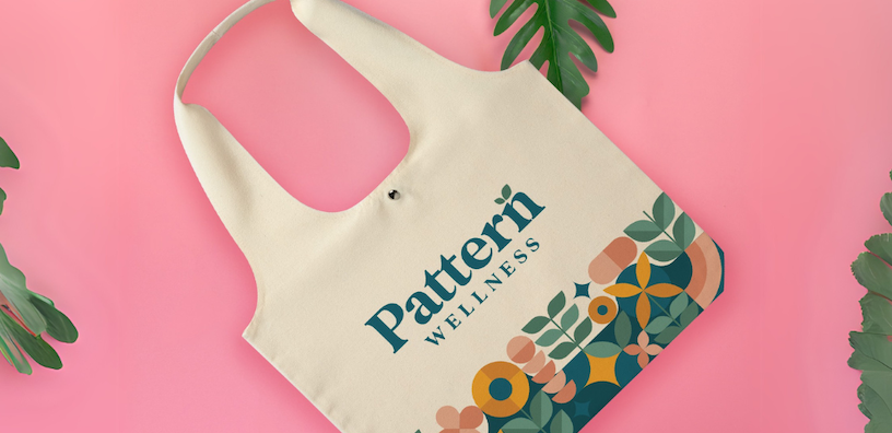 A branded tote bag for "Pattern Wellness" featuring their logo and a nature-inspired design against a pink backdrop.