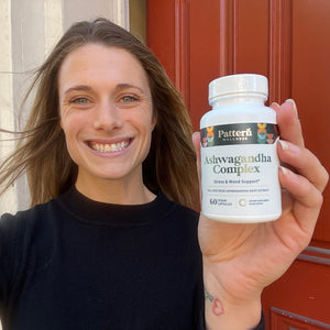 A female customer with a cheerful expression, showcasing a bottle of Pattern Wellness Ashwagandha Complex.