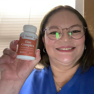 A female customer with a cheerful expression, showcasing a bottle of Pattern Wellness Zinc Complex.