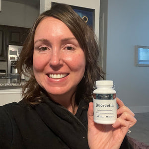 A female customer with a bright smile holding a bottle of Pattern Wellness Quercetin.