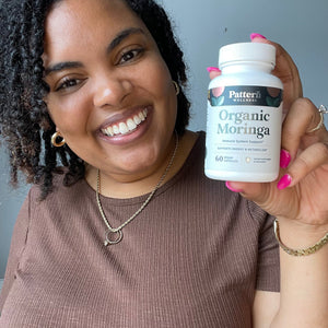 A cheerful customer, showcasing a bottle of Pattern Wellness Organic Moringa.