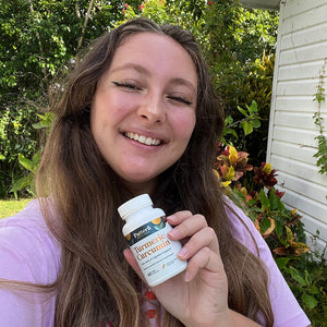 A female customer with a bright smile holding a bottle of Pattern Wellness Turmeric Curcumin.