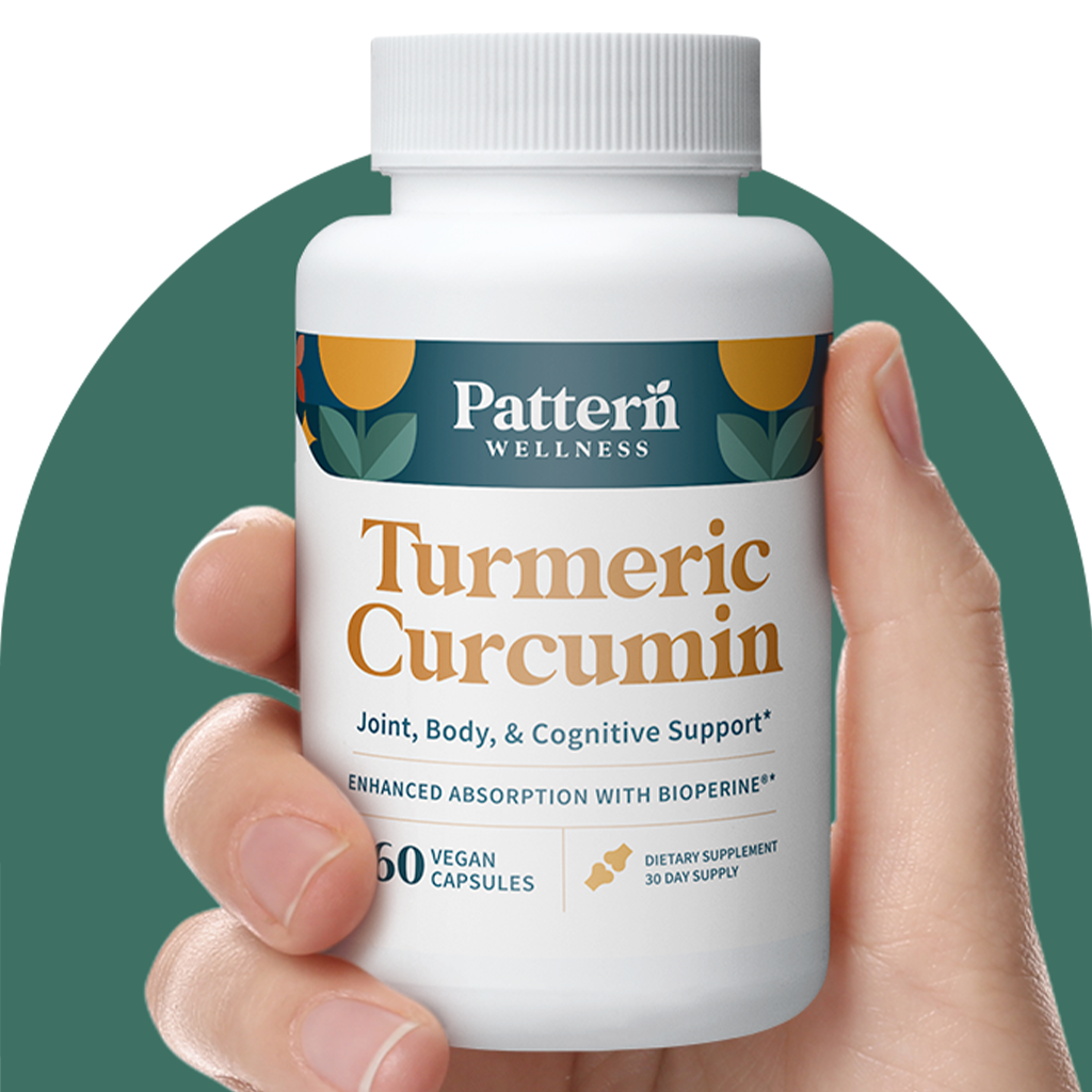 A hand holding a bottle of Pattern Wellness Turmeric Curcumin.