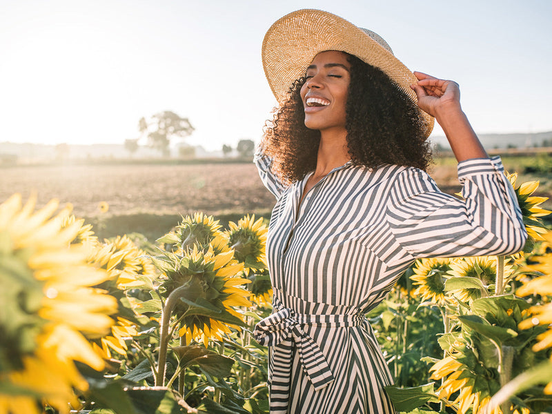 In a field of sunflowers, a woman with a hat enjoys the beauty of nature.