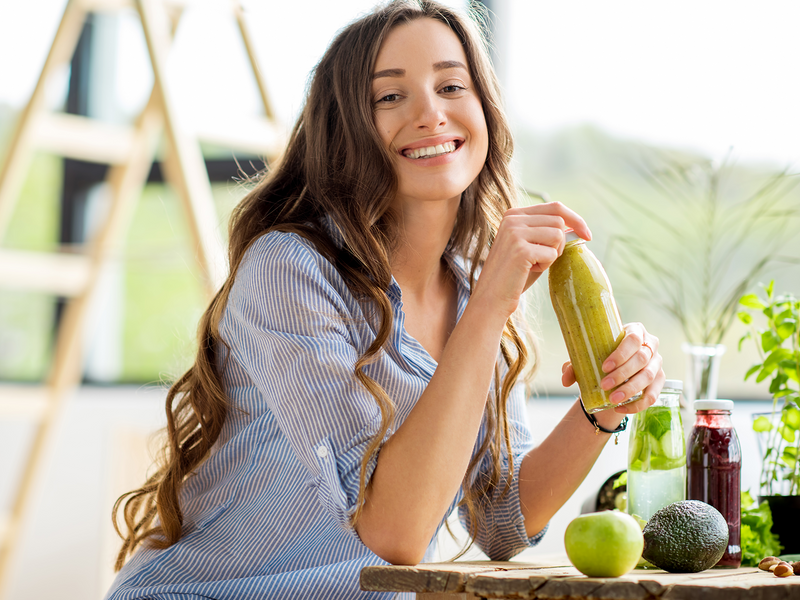 A cheerful woman holds a green smoothie.