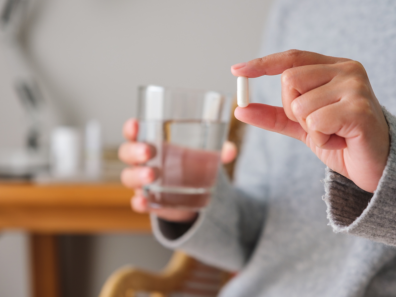 A person is holding a pill in one hand while grasping a glass of water.