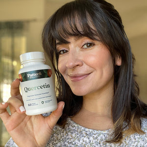 A female customer smiling while holding a bottle of Pattern Wellness Quercetin.