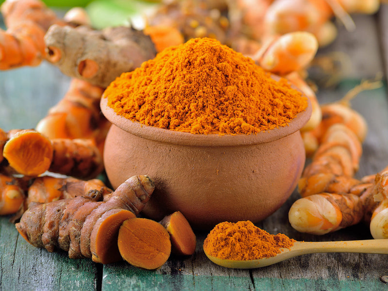 Fresh turmeric roots next to a bowl filled with bright yellow turmeric powder.