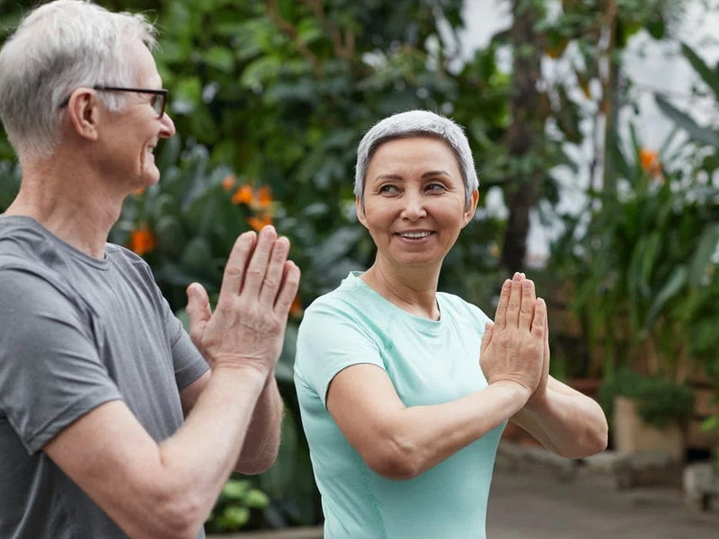 An older couple practicing yoga together in a serene garden.