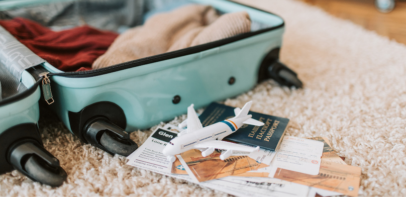 Open suitcase with travel essentials, toy airplane, passports, and boarding passes on a soft carpet.