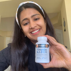 A female customer with a bright smile holding a bottle of Pattern Wellness Vitamin K2 & D3.