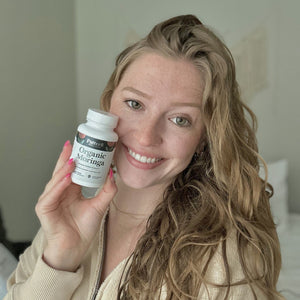 A female customer smiling while holding a bottle of Pattern Wellness Organic Moringa.