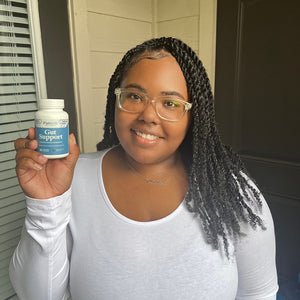 A female customer with a bright smile holding a bottle of Pattern Wellness Gut Support.