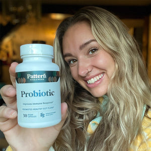 A female customer with a bright smile holding a bottle of Pattern Wellness Probiotic.