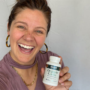 A female customer smiling while holding a bottle of Pattern Wellness Organic Garlic.