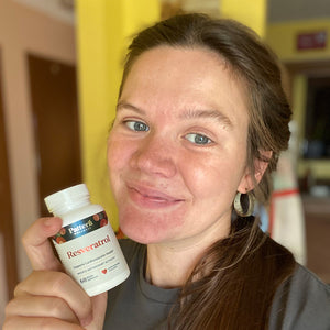 A female customer with a bright smile holding a bottle of Pattern Wellness Resveratrol.