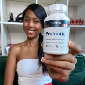 A female customer with a cheerful expression, showcasing a bottle of Pattern Wellness Probiotic.