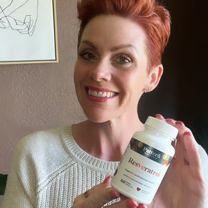 A female customer with a cheerful expression, showcasing a bottle of Pattern Wellness Resveratrol.