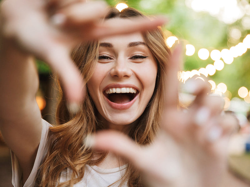 A woman smiling brightly while making a cheerful hand gesture.