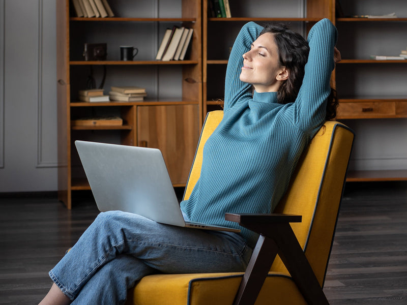 A woman comfortably sitting in a chair, using her laptop, immersed in her tasks.