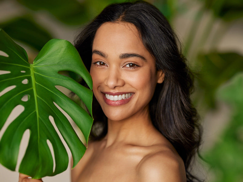 A woman smiles brightly while holding a vibrant green leaf.