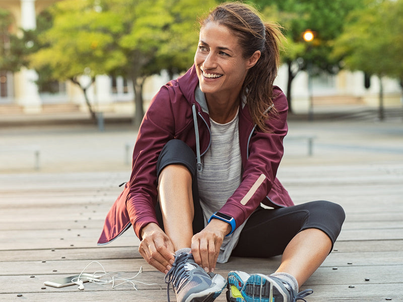 A woman is seated carefully tying her shoes.