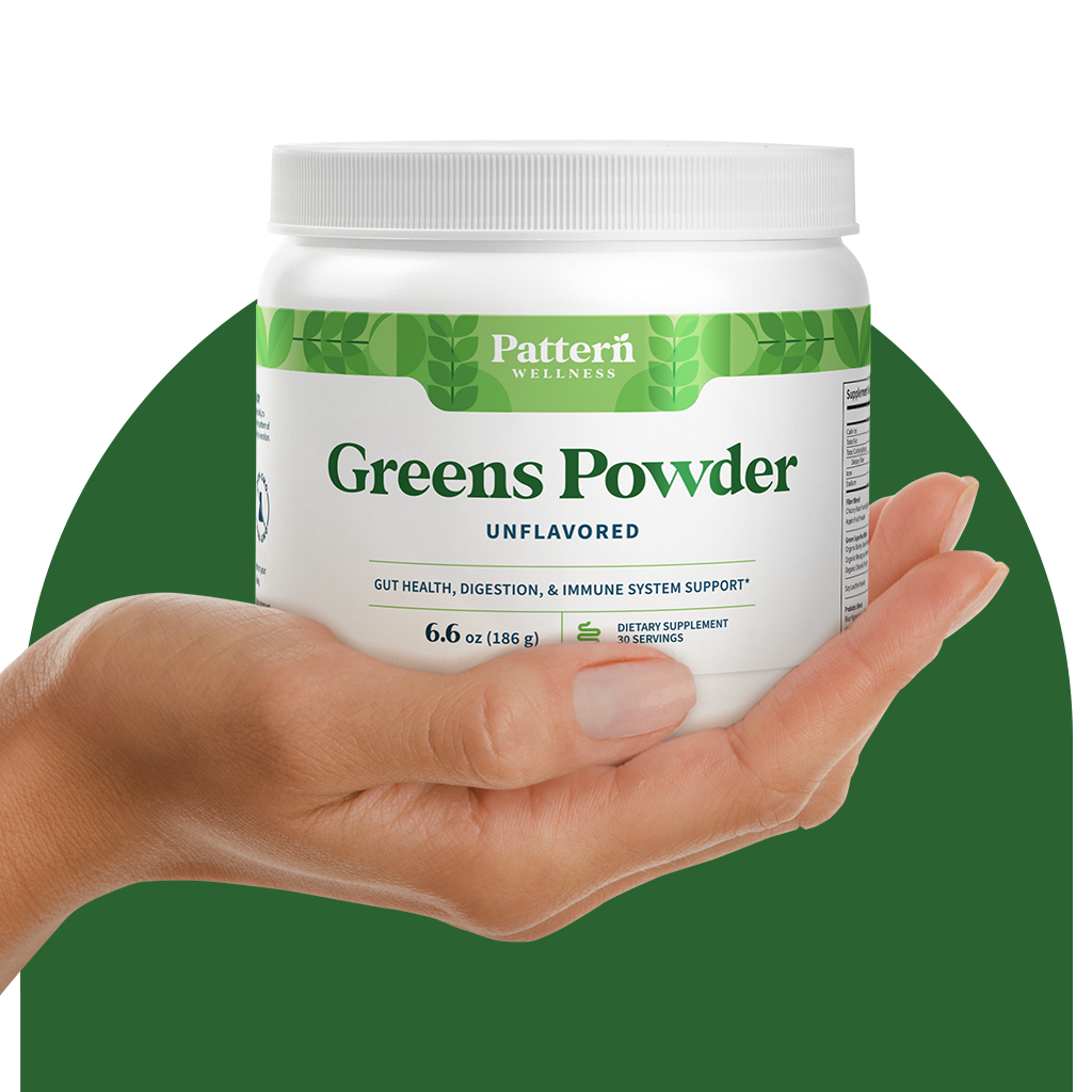 A hand holding a jar of Pattern Wellness Greens Powder.