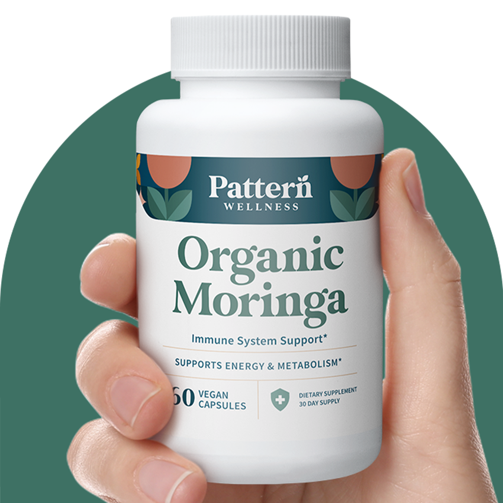 A hand holding a bottle of Pattern Wellness Organic Moringa.