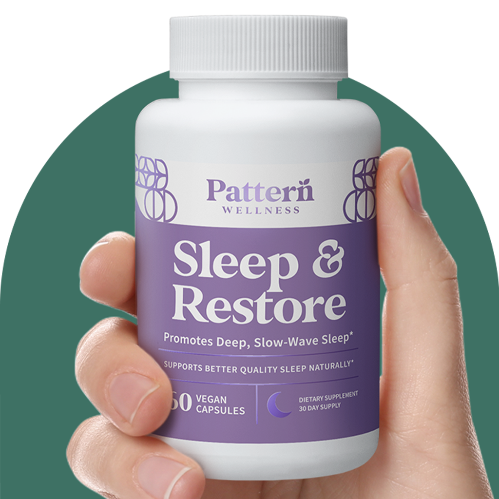 A hand holding a bottle of Pattern Wellness Sleep + Restore.