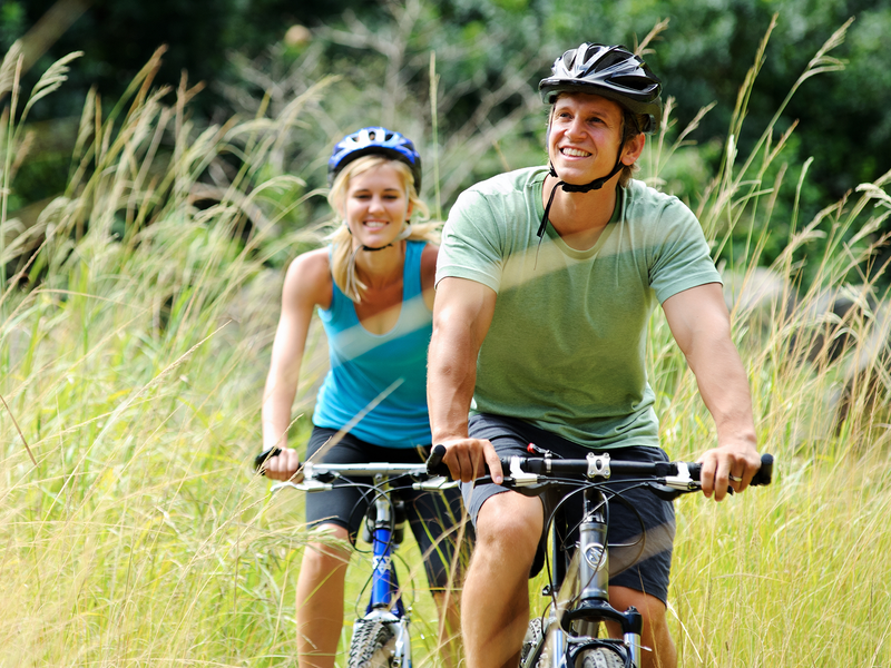 A couple riding bicycles amidst tall grass.