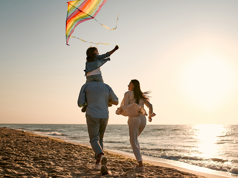 A family joyfully flying a colorful kite on a sunny beach.