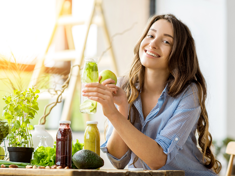 A woman is holding a glass of juice, smiling as she enjoys a refreshing drink.