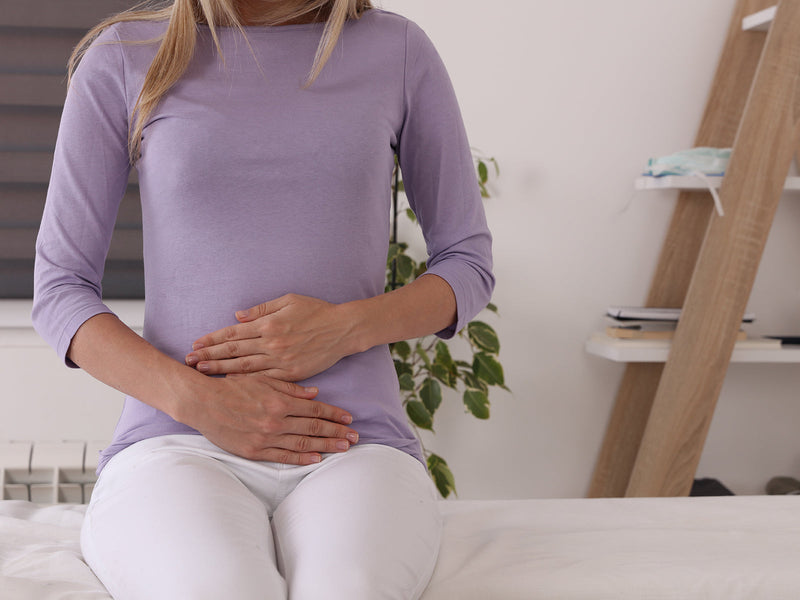 A woman sitting on a bed, holding her stomach.