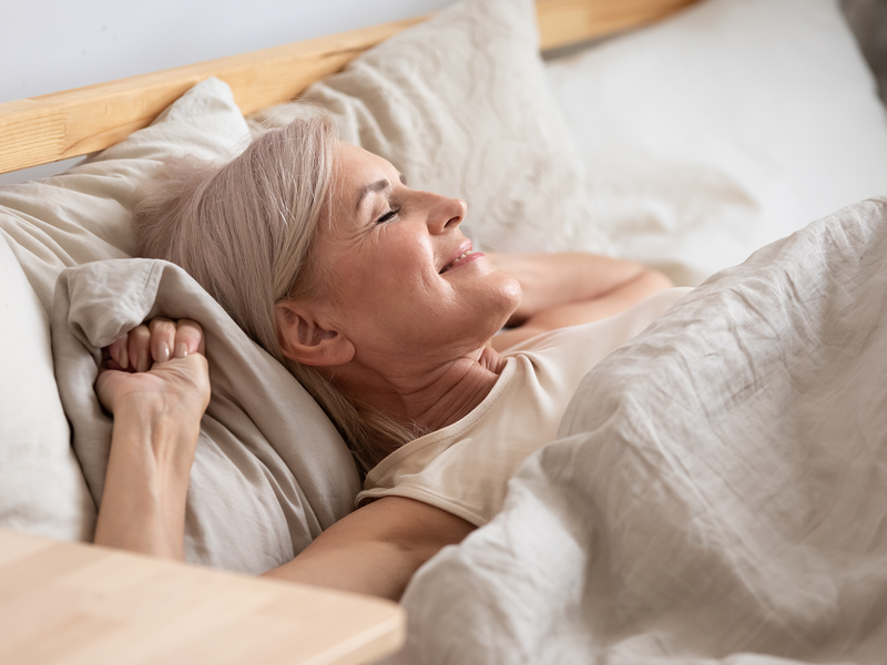 A woman lies peacefully in bed with her eyes gently closed.