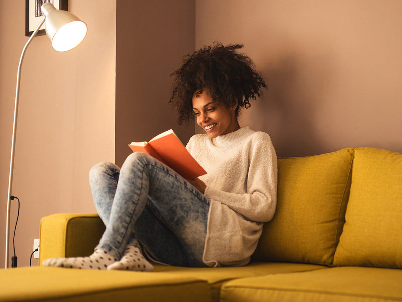 A woman seated on a couch, engrossed in reading a book.