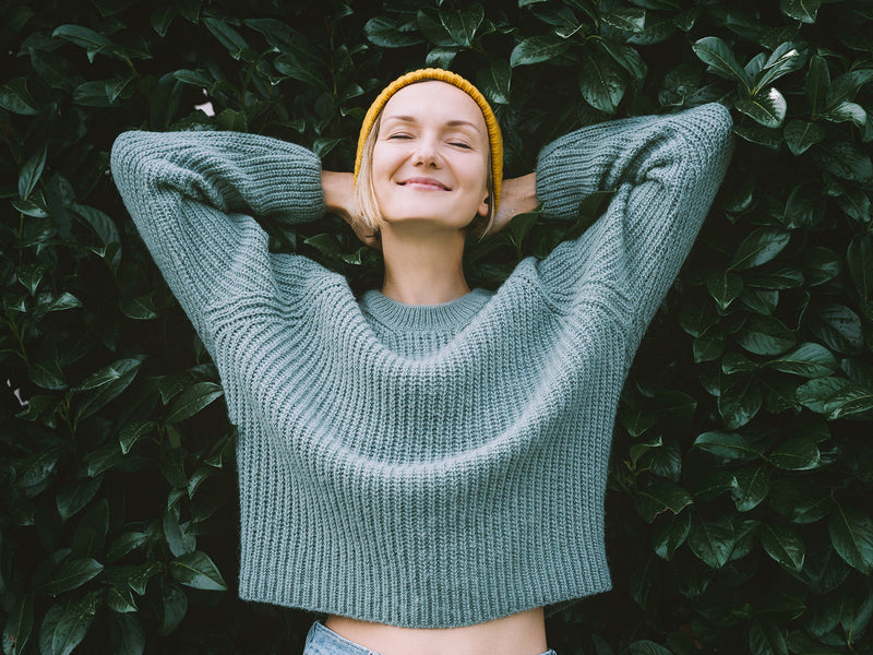 A cheerful woman stands before vibrant green leaves.