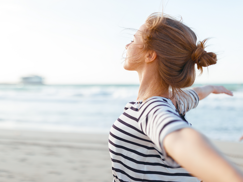 A woman on the beach extends her arms wide.