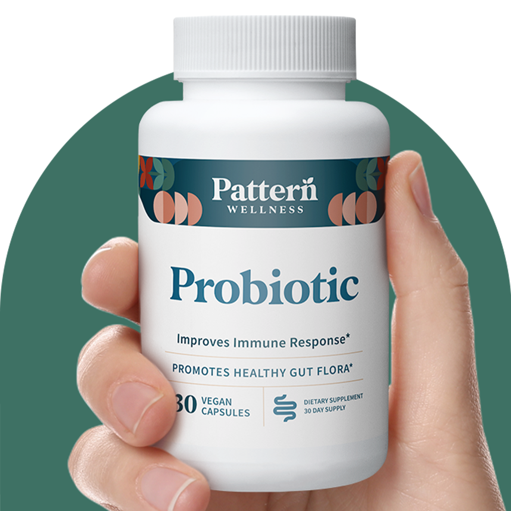 A hand holding a bottle of Pattern Wellness Probiotic.