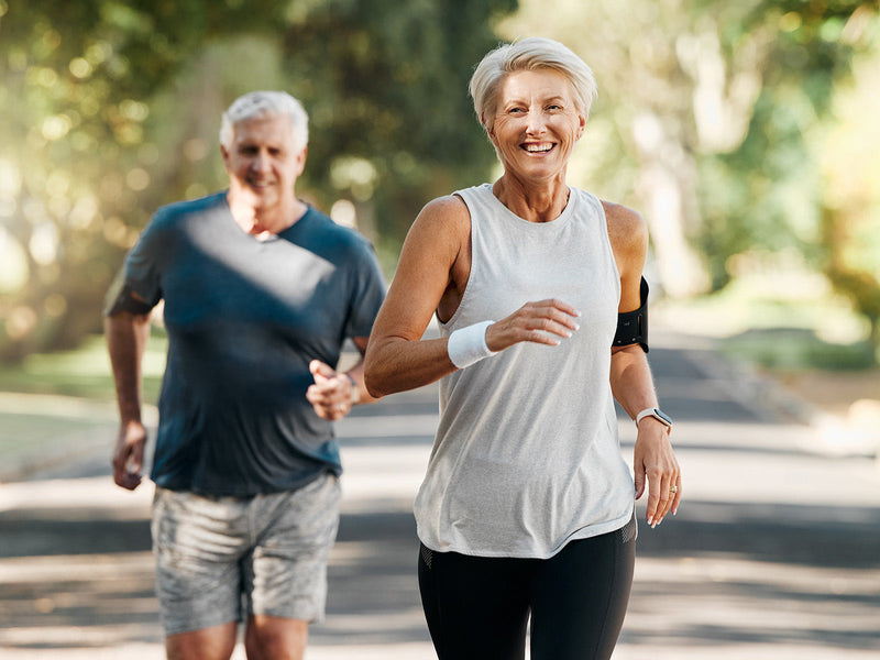 An older couple jogging together on a scenic road.