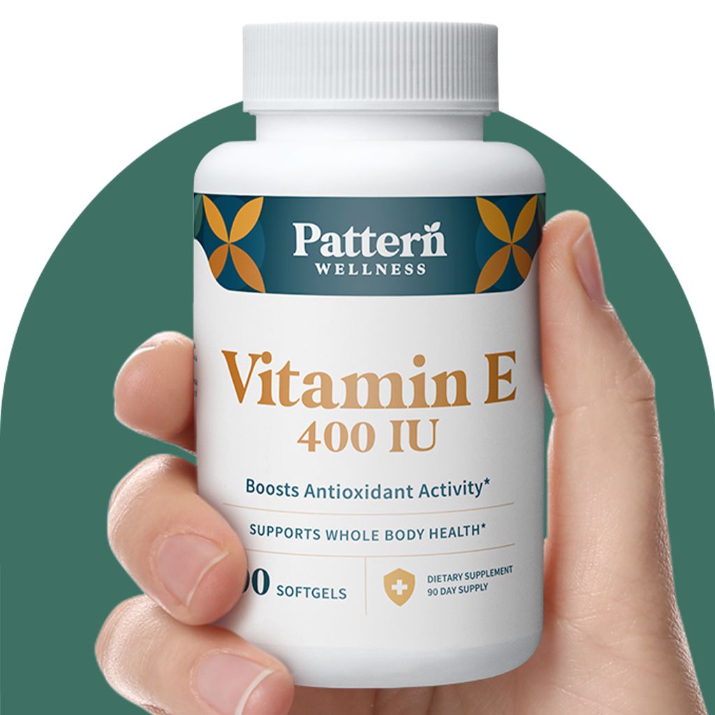 A hand holding a bottle of Pattern Wellness Vitamin E.