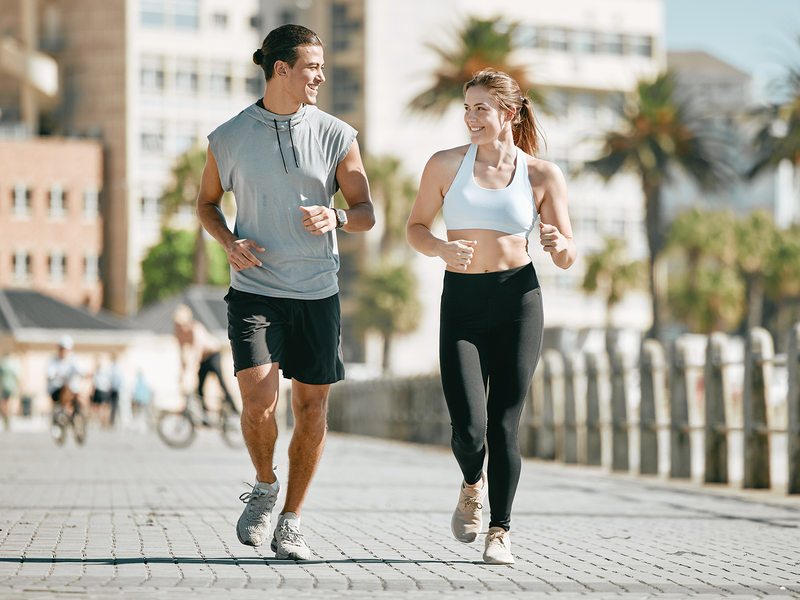 A man and woman jogging side by side on a sidewalk.