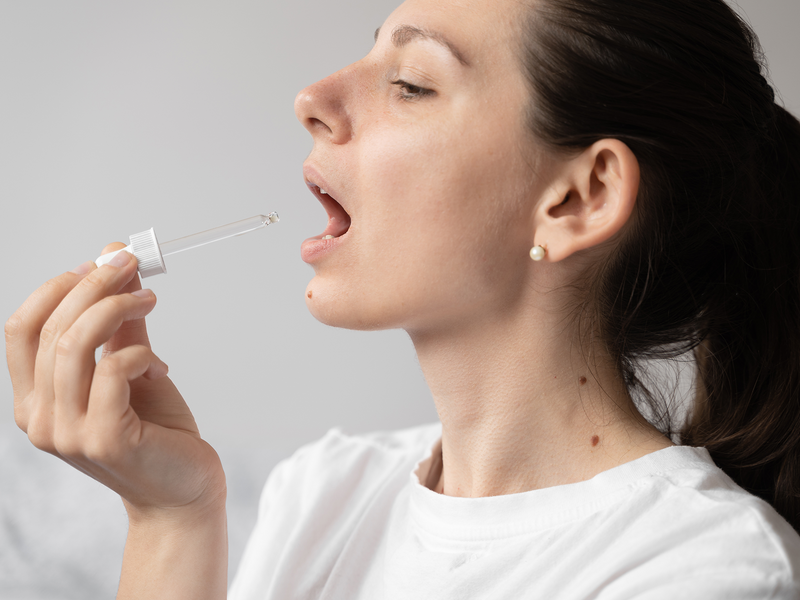 A woman is using a medicine dropper to take her vitamins.