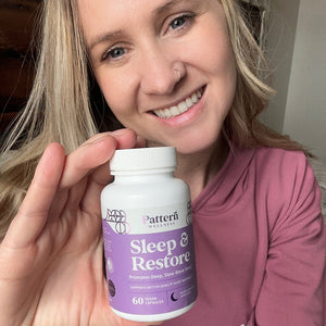 A female customer with a bright smile holding a bottle of Pattern Wellness Sleep + Restore.