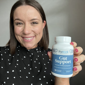 A female customer with a cheerful expression, showcasing a bottle of Pattern Wellness Gut Support.