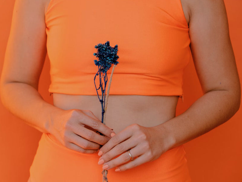 A woman in an orange top holds a blue flower.